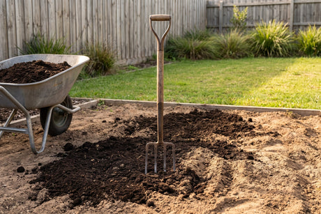 Garden fork working dark compost into a freshly dug garden bed