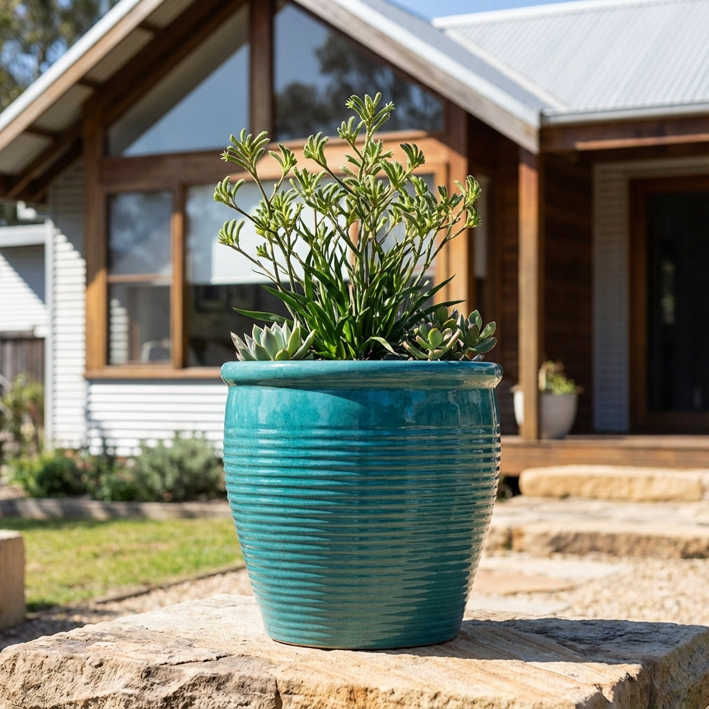 A Forest Green Holland Planter (available in various sizes) sits on a stone step outside a modern house with large windows, bringing a natural touch to the contemporary setting.