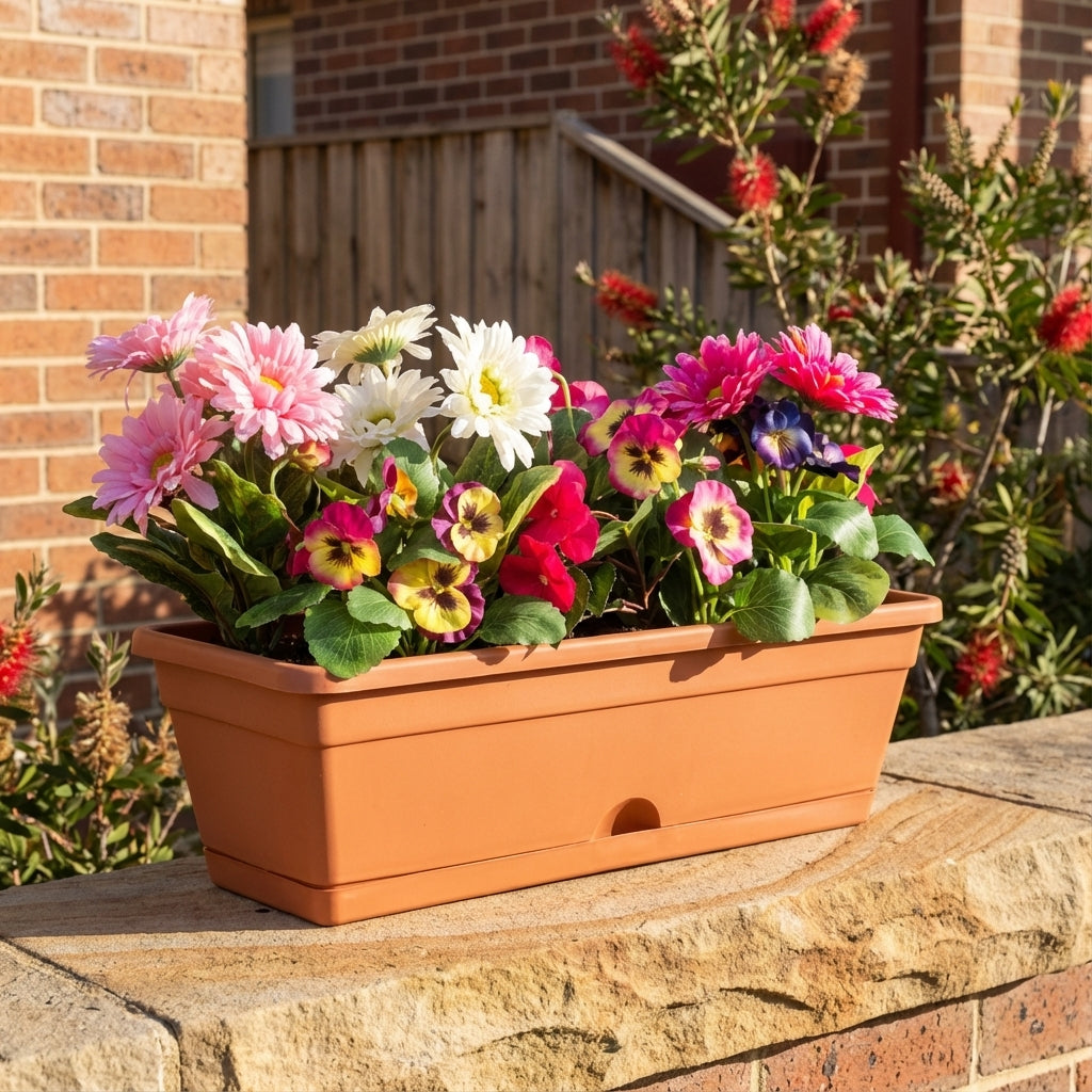 The Terracotta Outdoor Garden Up Classic Pot (495mm x 175mm) with vibrant flowers rests on a stone ledge in a sunlit garden.