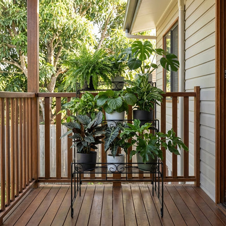 Potted houseplants on a 3 Tier Outdoor Heavy Duty Plant Stand create a stunning vertical plant display on a wooden porch beside the house.