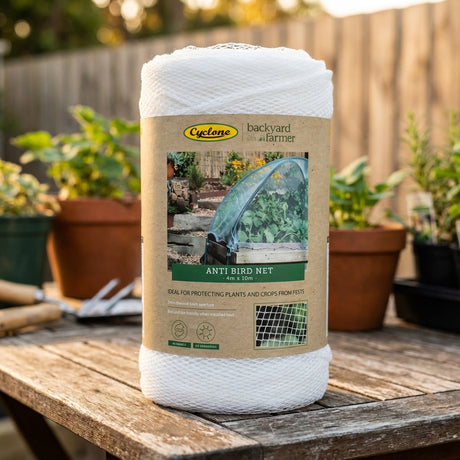 A roll of Backyard Farmer 4 x 10m x 5mm Anti Bird Net sits on a wooden table with potted plants nearby—perfect fruit tree protection using bird-friendly mesh.