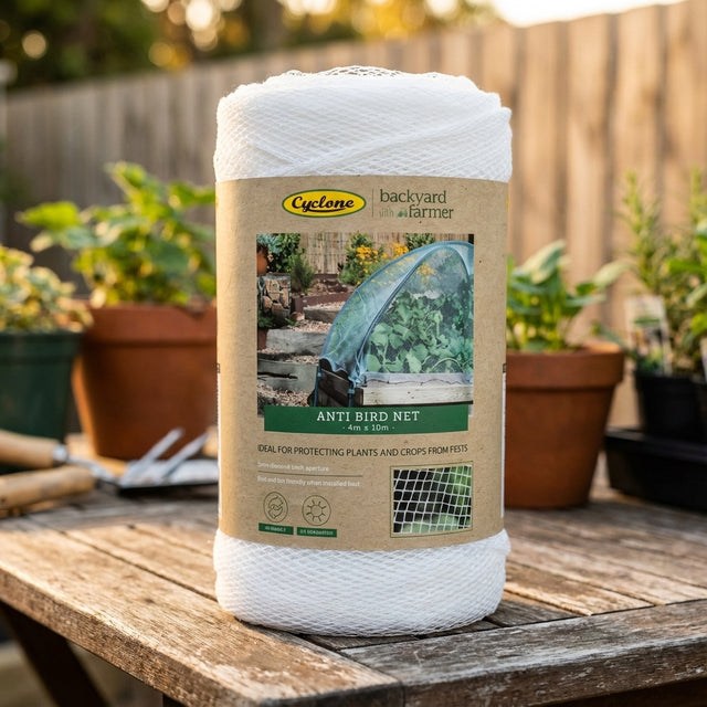 A roll of Backyard Farmer 4 x 10m x 5mm Anti Bird Net sits on a wooden table with potted plants nearby—perfect fruit tree protection using bird-friendly mesh.
