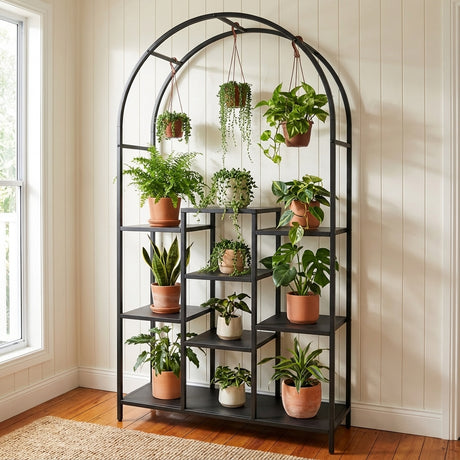 The Black Mona Arched Metal Plant Stand displays various potted houseplants, including some hanging, by a sunlit window in a cozy room.