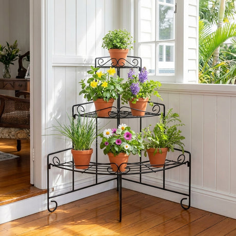 The Corner Heavy Duty Plant Stand - 880mm x 580mm, in black, holds six potted flowering and green plants by a sunny window in a bright room.