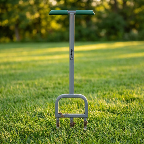 The Cyclone 3 Prong Lawn Aerator, featuring a green handle, stands upright on a lawn. It's designed to reduce soil compaction, with trees offering a lush background.
