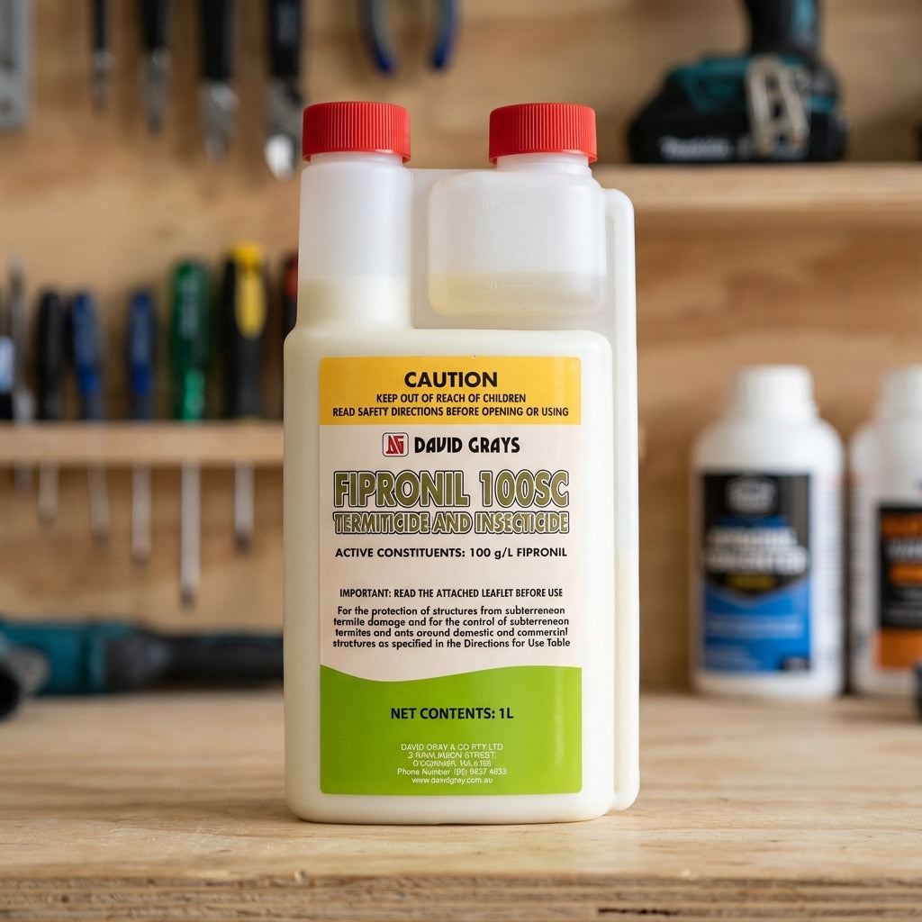 A 1L bottle of David Grays Fipronil Concentrate for termite and ant control rests on a wooden workbench, with other bottles blurred in the background.