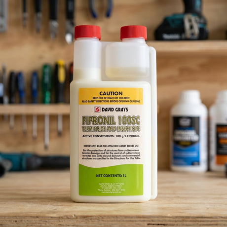 A 1L bottle of David Grays Fipronil Concentrate for termite and ant control rests on a wooden workbench, with other bottles blurred in the background.