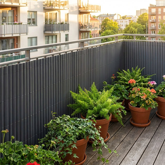 A 50 x 50 x 69cm green bird bath is surrounded by potted plants on a wooden balcony, with buildings and trees in the background at sunset.