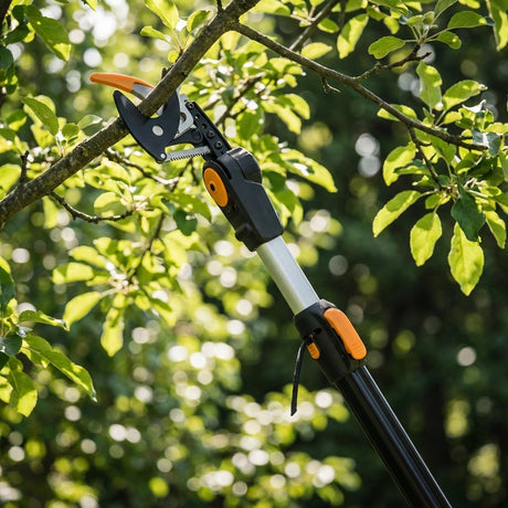 The Fiskars PowergearX Telescopic Tree Pruner trims branches among green leaves in a sunny garden, making pruning easy and efficient.