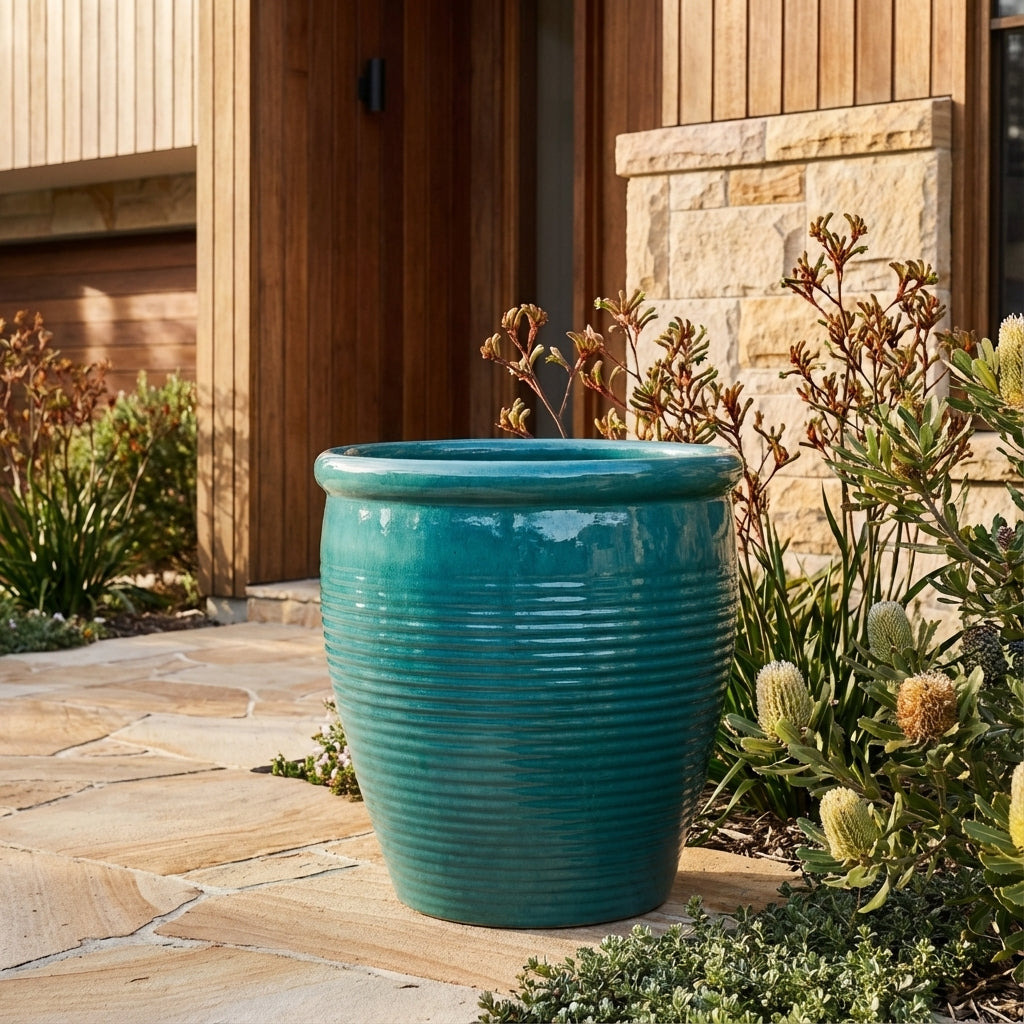 A Forest Green Holland Planter in a large size sits on a stone patio near plants and a modern wooden house.