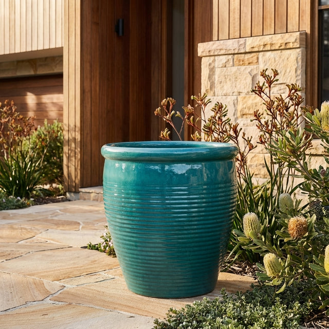 A Forest Green Holland Planter in a large size sits on a stone patio near plants and a modern wooden house.