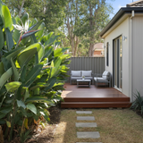 Small backyard deck with outdoor seating and lush greenery. A Giant White Bird of Paradise - Strelitzia Nicolai stands out as a feature plant, providing a natural tropical privacy screen for relaxing by the wooden fence.