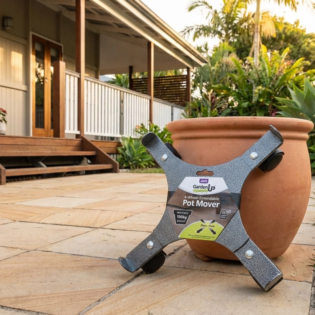 The Heavy Duty Extendable Pot Mover (330mm–510mm) with lockable castors is placed beside a large potted plant on a tiled patio outside a house.