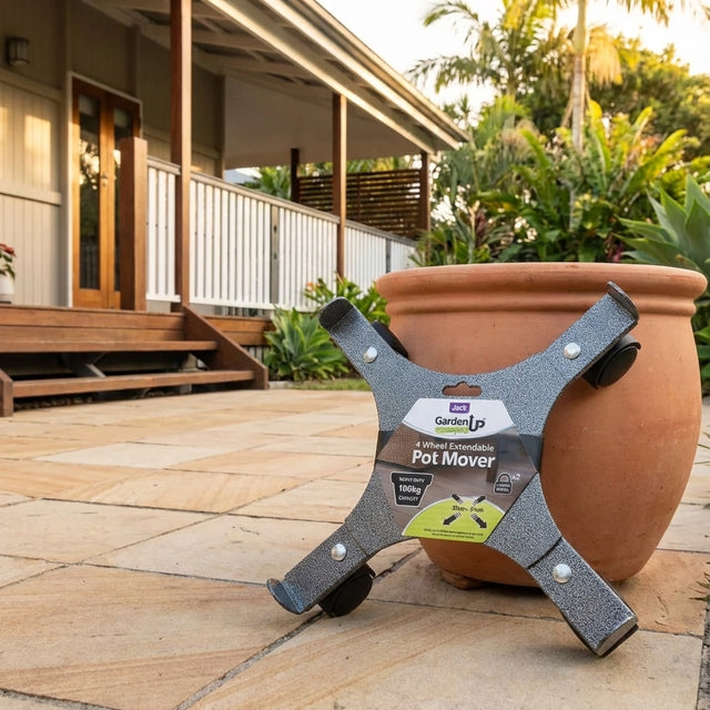 The Heavy Duty Extendable Pot Mover (330mm–510mm) with lockable castors is placed beside a large potted plant on a tiled patio outside a house.
