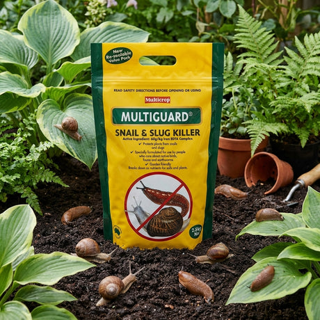 The Multicrop 2.5kg Multiguard Snail and Slug Killer sits in a garden bed among snails and lush plants, providing a wildlife-friendly way to protect your garden.