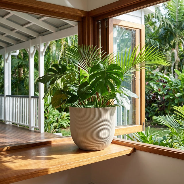 A monstera and palm plant in a Mushroom Beige Sereh Pot sit on a wooden windowsill, with a garden visible through the open window. Various sizes available.