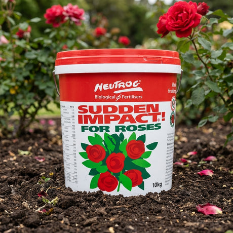 A 10kg tub of Neutrog Sudden Impact For Roses Fertiliser sits on garden soil among blooming red roses.