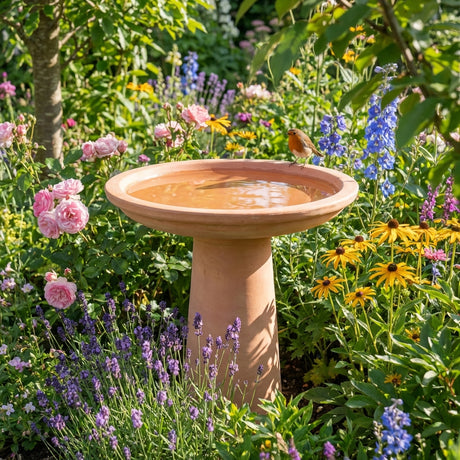 The Northcote Pottery Antique White Cafestyle Villa Bird Bath (37 x 47cm) stands among vibrant flowers, with a small bird perched on its edge.