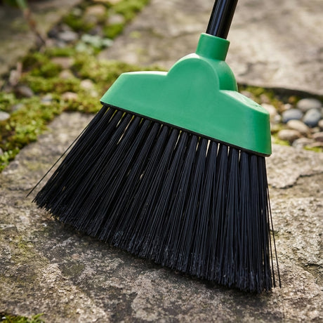 The Oates Slimline Sweep Handled Outdoor Broom, with stiff bristles, efficiently sweeps moss and small stones from stone pavement.