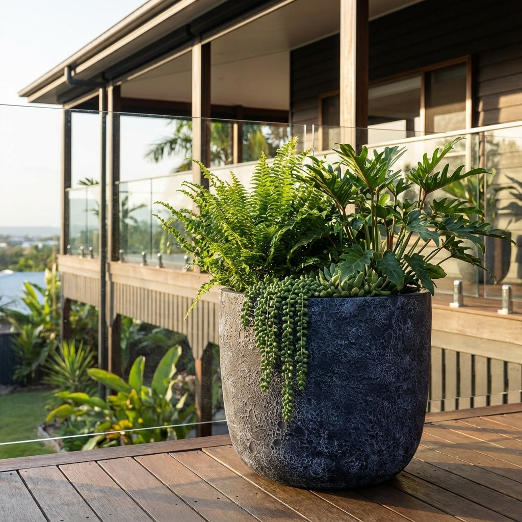 Large outdoor planter with lush green plants on a wooden deck near a modern house, featuring the stylish Pierre U Pot Black (various sizes available) crafted from lightweight fibre cement.