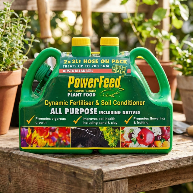 The PowerFeed 2 x 2L Hose On Liquid Fertiliser - Twin Pack, featuring green containers with yellow lids and caps, sits on a wooden surface—ideal for storing liquid fertiliser.