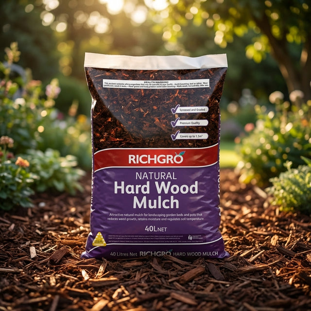A bag of Richgro 40L Hard Wood Mulch sits on a garden bed among plants and sunlight, providing excellent moisture retention as a premium garden mulch.