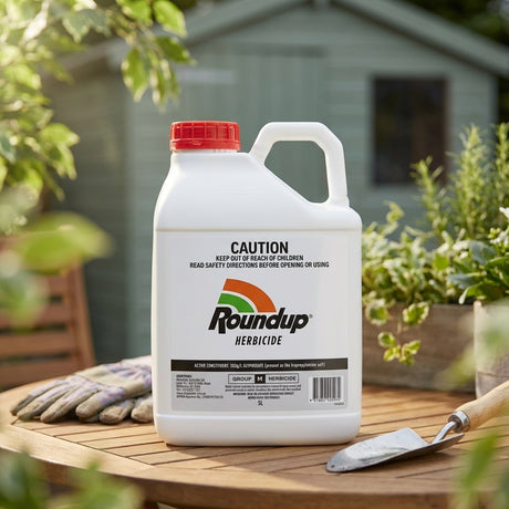 A Roundup 5L Herbicide Liquid Concentrate Weedkiller sits on a wooden table outdoors, alongside gardening gloves and a trowel—ideal for tackling large-scale weed control in your garden.