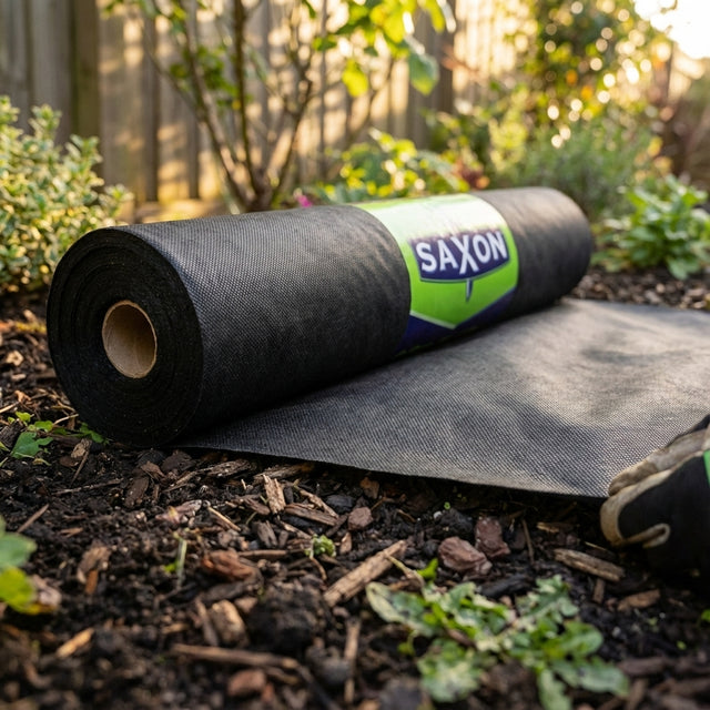 A Saxon 0.9 x 10m Non Woven Weed Control Mat being unrolled on garden soil, with nearby plants in the backyard.