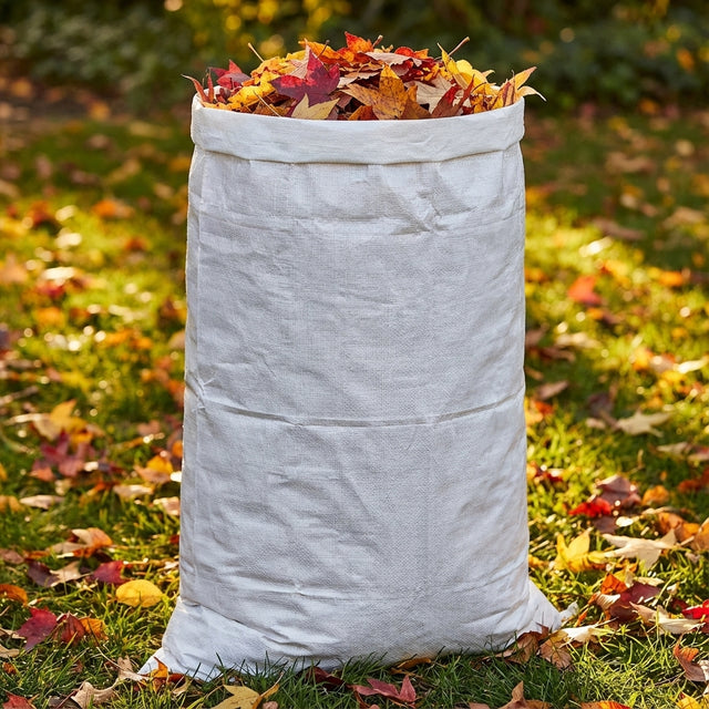 A Saxon 150L Garden Bag from the 3 Pack is filled with colorful autumn leaves and stands on a lawn covered in fallen leaves.