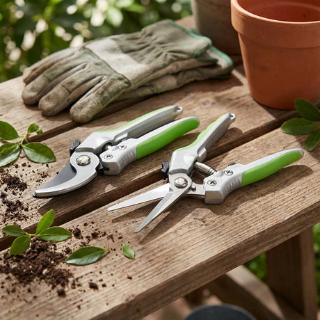 The Saxon 2 Piece Pruning Set, including garden shears and gloves, is displayed on a wooden table scattered with soil, leaves, and a flowerpot.