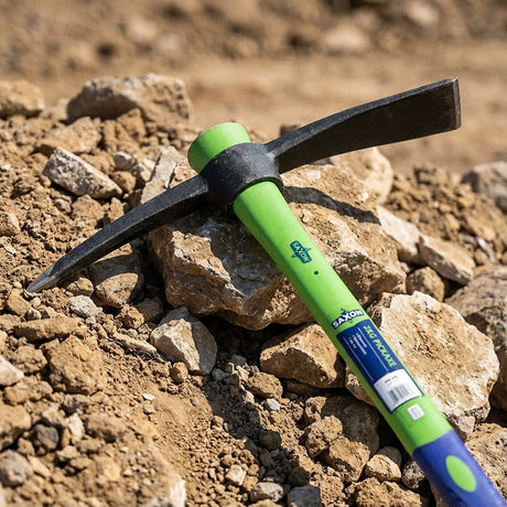 The Saxon Fibreglass Pickaxe - 2kg, with its green handle, lies on a pile of rocks and dirt outdoors, highlighting its durability and reliability as an essential landscaping tool.