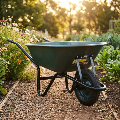 A green wheelbarrow on a garden path surrounded by flowers and plants in sunlight, with a Holman Professional Rain Gauge Cylinder nearby for accurate rainfall measurement.