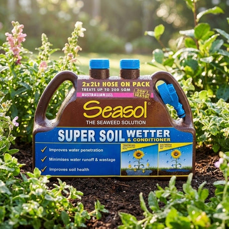 The Seasol 2 x 2L Hose On Super Soil Wetter and Conditioner Twin Pack sits in a garden of green plants and flowers, showcasing its liquid seaweed formula for improved soil health.