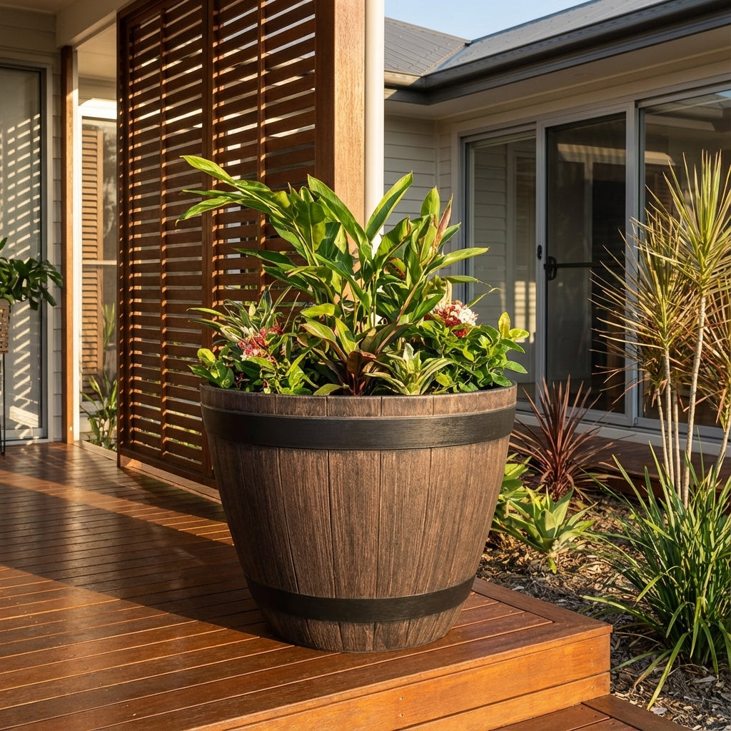 The Wine Barrel Planter - 800mm, filled with lush green plants, sits on a wooden deck beside a modern house with sliding doors.