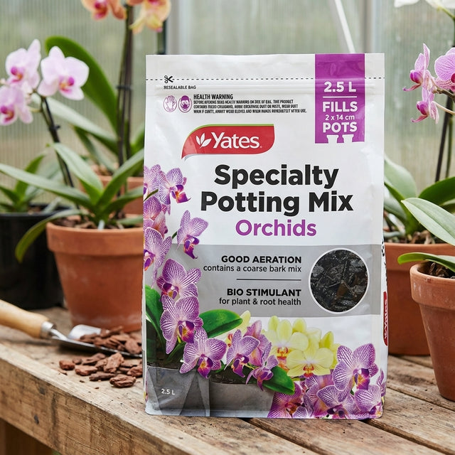 A bag of Yates 2.5L Specialty Potting Mix Orchids rests on a wooden table among potted orchids, its coarse bark blend perfect for healthy orchid roots.