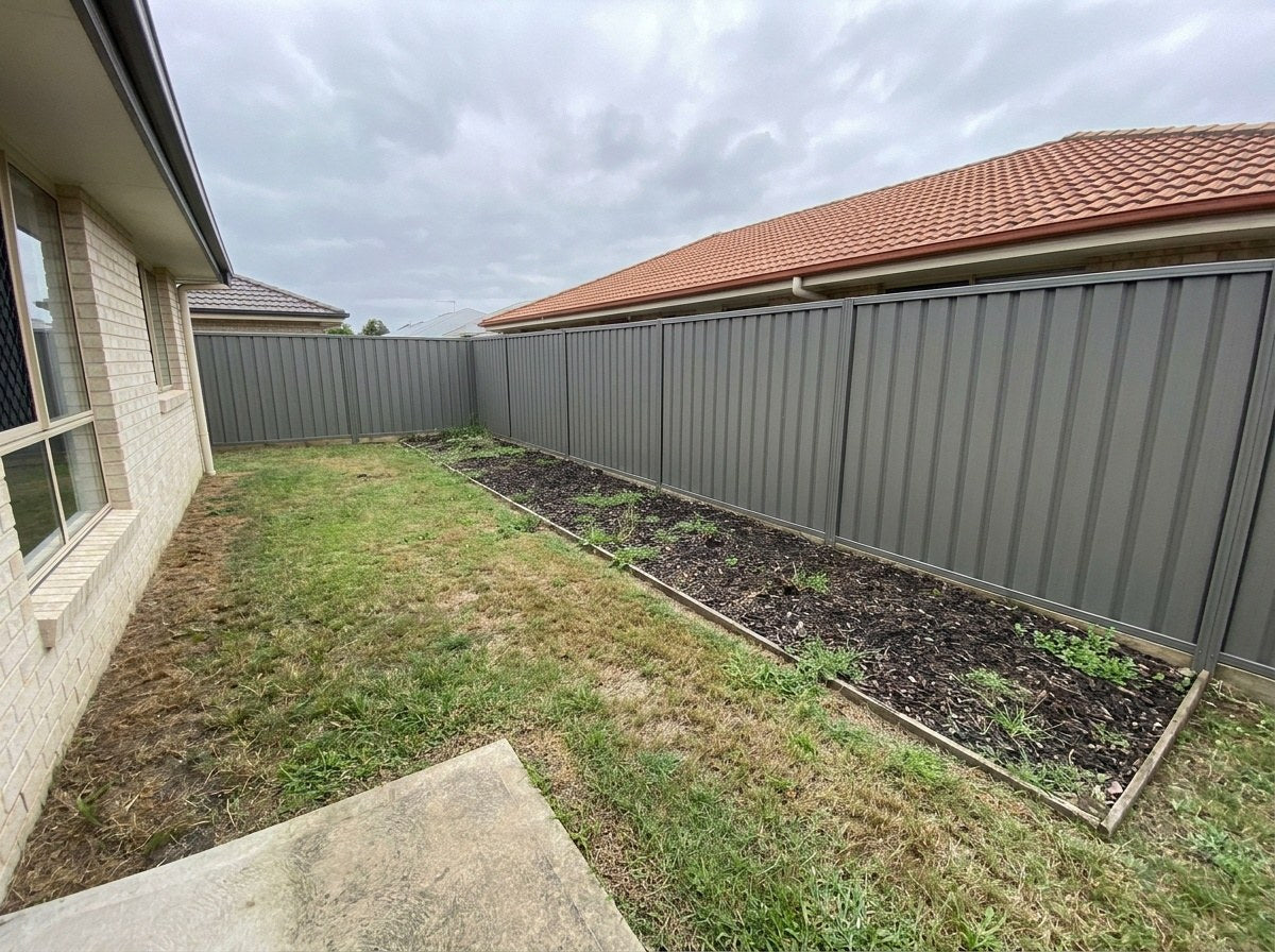 The same backyard before planting: a bare mulch bed along a Colorbond fence